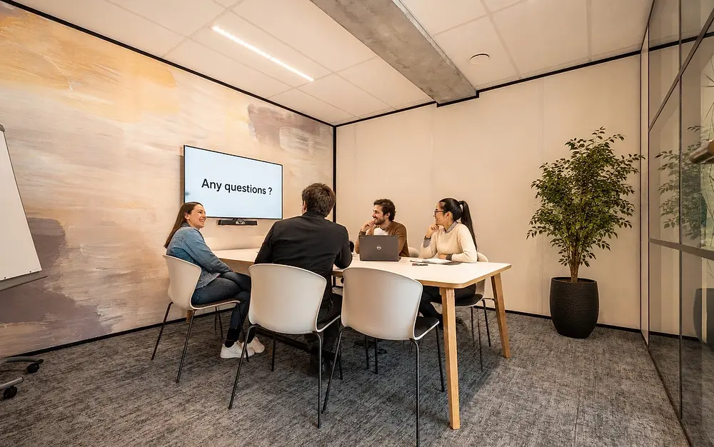 Un échange autour d'une table, devant un écran affichant « Any questions ? »